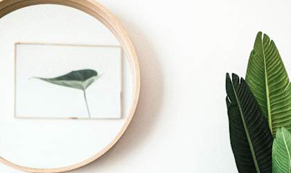 a round mirror hanging on a white wall above a dresser with a green plant