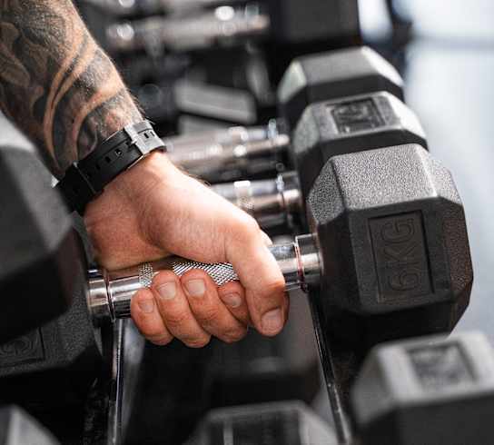 A man's hand with a watch is holding a dumbbell in a gym.