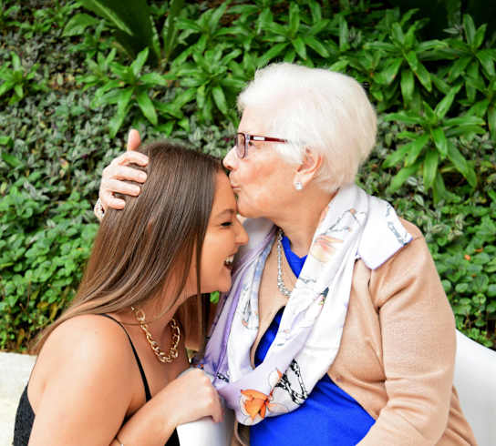 A woman in a blue top and white pants is giving a kiss to a woman in a floral dress at Nook at Northaven Apartments, Washington, 98125