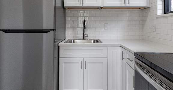 A kitchen with a refrigerator, sink, and cabinets.