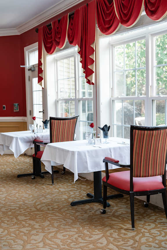 A dining room with red chairs and white tablecloths.