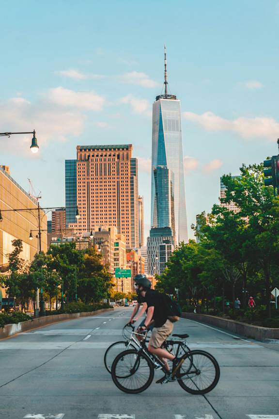 A man riding a bike on a city street with tall buildings in the background at Aria, New York.