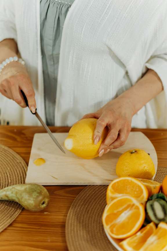 A person cutting a lemon on a wooden cutting board.