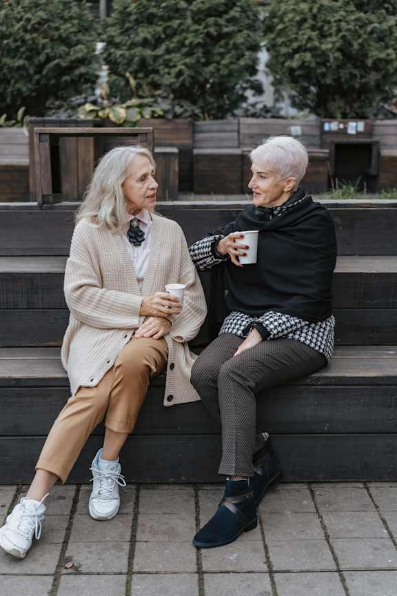 Two people sitting on a bench, one holding a cup.