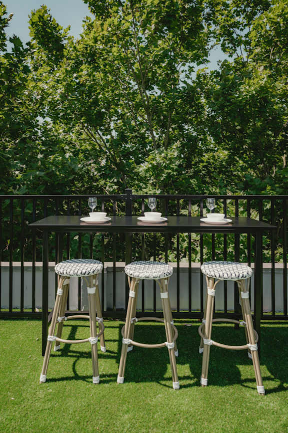 a bar table and stools on a lawn in front of a fence