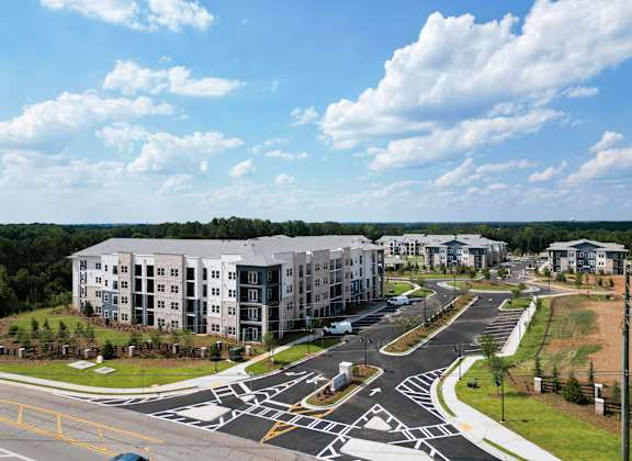 A car is parked in a parking lot in front of apartment buildings at The Crest at South Point Apartments, McDonough, GA, 30253