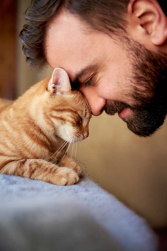 Man Smiling while Resting Forehead Against Orange Tabby Cat