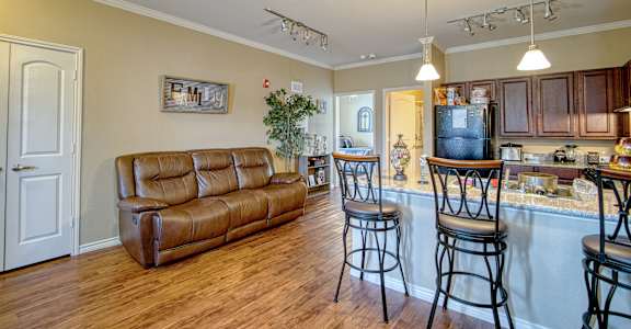 A kitchen with a bar and stools is adjacent to a living room with a couch and a plant.