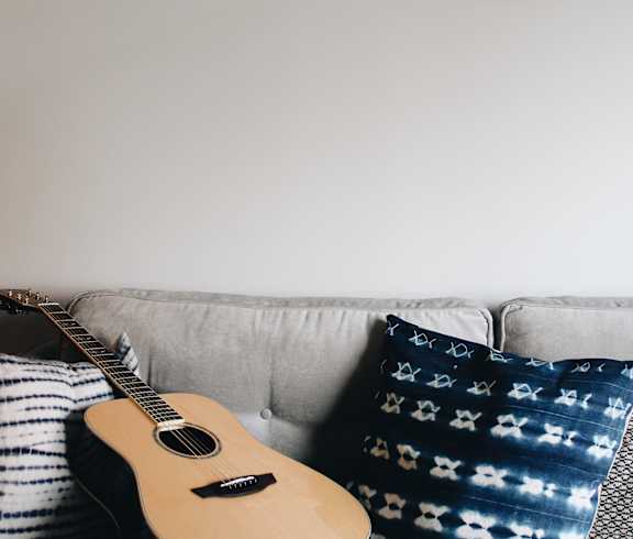 A guitar is placed on a couch with pillows.