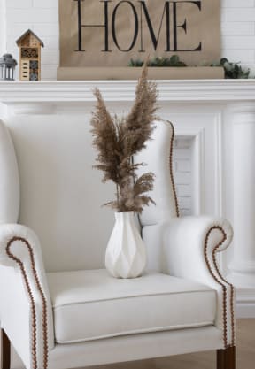 A white chair with a vase of dried flowers placed on the seat.