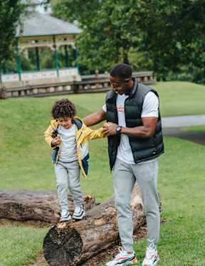 A man and a child are standing on a log in a park.