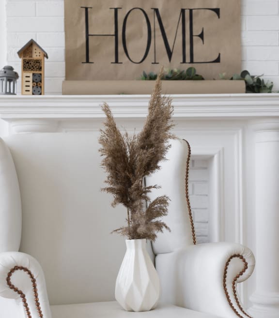 A white vase filled with flowers sitting on a white chair in a living room setting.