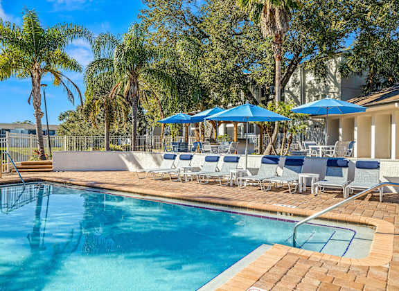 A pool surrounded by palm trees and blue umbrellas.
