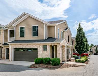 A two-story house with a garage is surrounded by a well-maintained lawn and a clear sky.