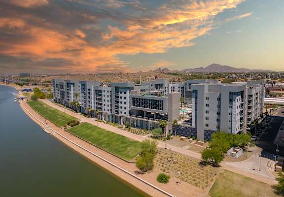 A modern apartment complex is situated along a riverbank with a mountain in the distance.