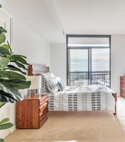 A bedroom with a bed, nightstand, and window overlooking a balcony.
