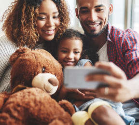 a family of three sitting on a couch with a teddy bear and looking at a phone