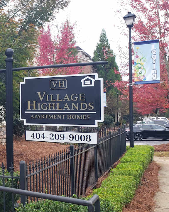 A sign for Village Highlands is in front of a black fence.