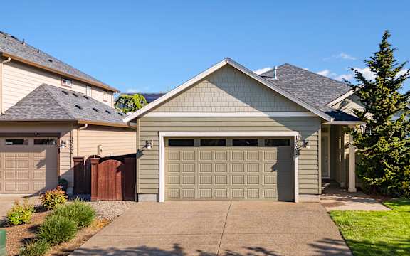 A house with a grey garage door is in front of a green lawn.