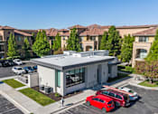 Thumbnail 27 of 28 - A red car is parked in front of a white building with a parking lot in front of apartment buildings. at Siena Villas Apartments, Orem, UT