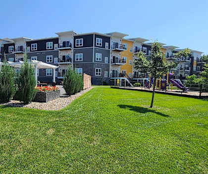 an apartment building with a green lawn and trees in front of it