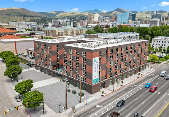 A large red brick building with a green sign on the side is in the middle of a busy street.