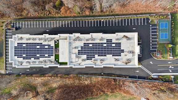 A parking lot with a building and solar panels on the roof.