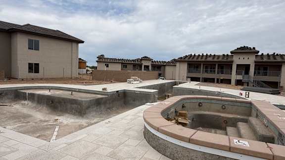 A construction site with a large building and a pool in the foreground.