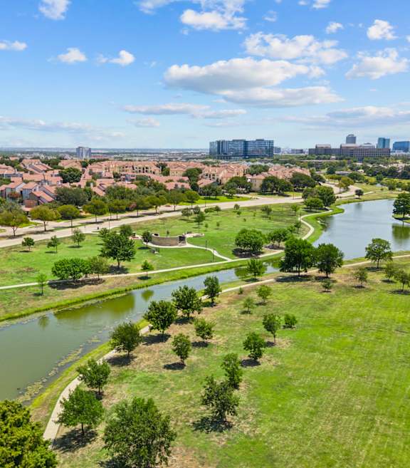 A river flows through a green field with trees and buildings in the background.