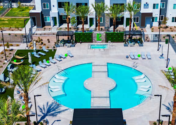 A large blue and white pool surrounded by palm trees and lounge chairs.