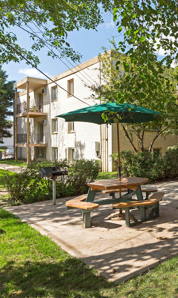 A sunny day at the outdoor seating area of a building with green umbrellas and picnic tables.
