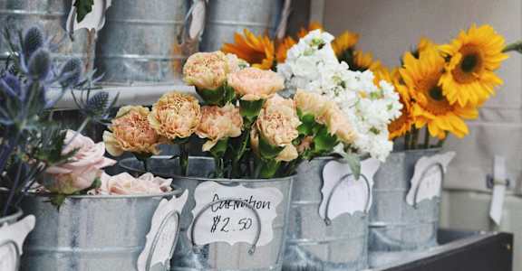 Sunflowers and other flowers are displayed in metal buckets for sale.