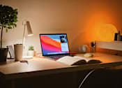Thumbnail 3 of 4 - A laptop is open on a desk with a book and a lamp beside it.