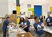 Thumbnail 3 of 5 - A group of people in blue shirts are packing items into boxes.
