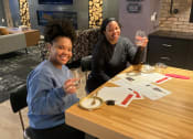 Thumbnail 3 of 7 - two women sitting at a table holding up glasses of wine