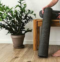 A person is sitting on a bench with a rolled-up yoga mat and a potted plant beside them.