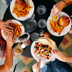 people sitting around a table eating food with burgers and fries
