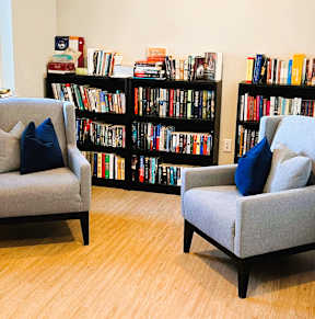 Two grey chairs with blue pillows in front of a bookshelf.