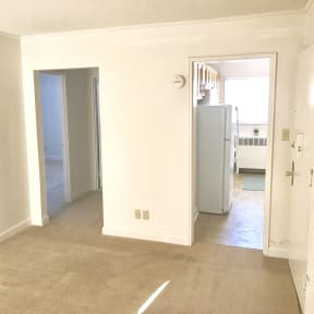 an empty living room with white walls and a door to a bedroom and a refrigerator