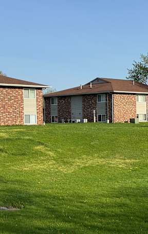 A grassy field with three apartment buildings in the background.