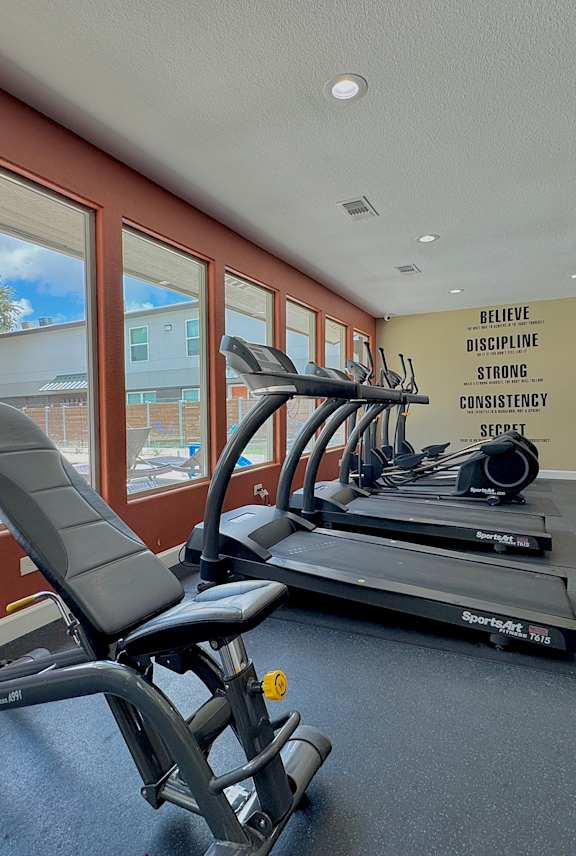 A gym with a row of treadmills and a motivational wall slogan.