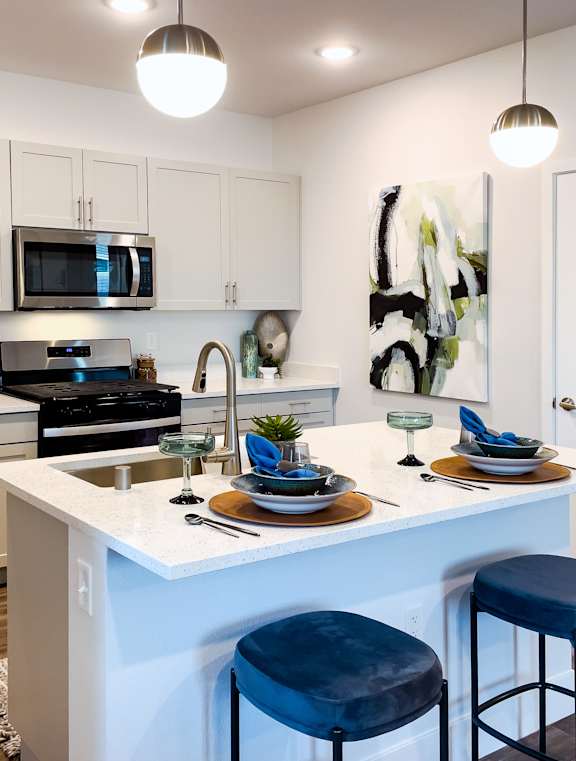 A modern kitchen with a white island and blue stools.