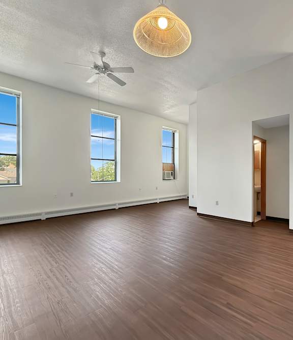 an empty living room and kitchen with wood floors and a ceiling fan