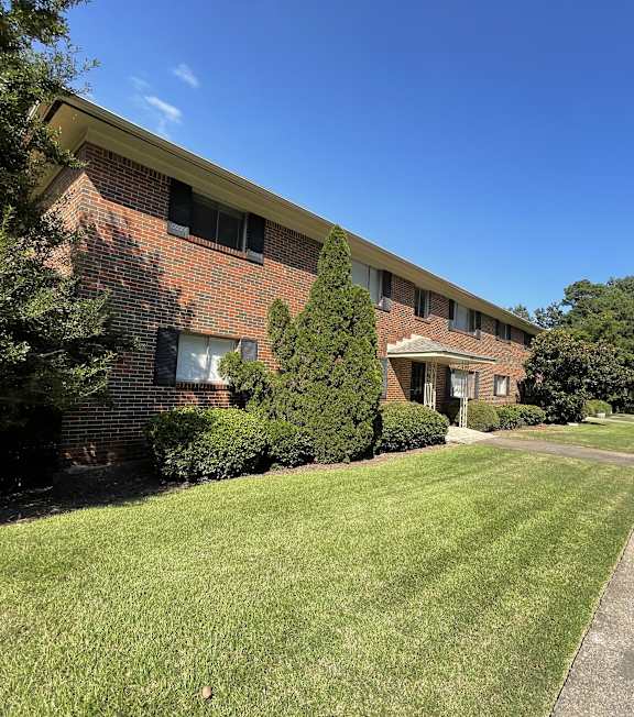 a large brick building with a green lawn and trees