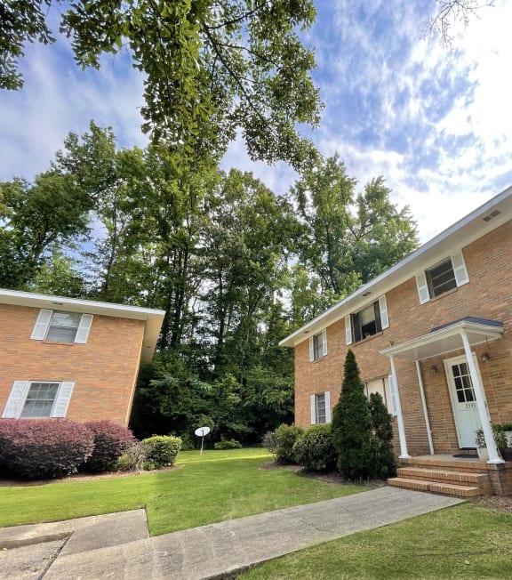 the front of a brick apartment building with a lawn and trees