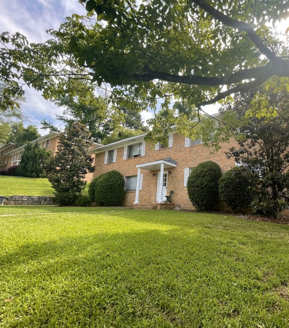 the front of a brick house with a lawn and trees