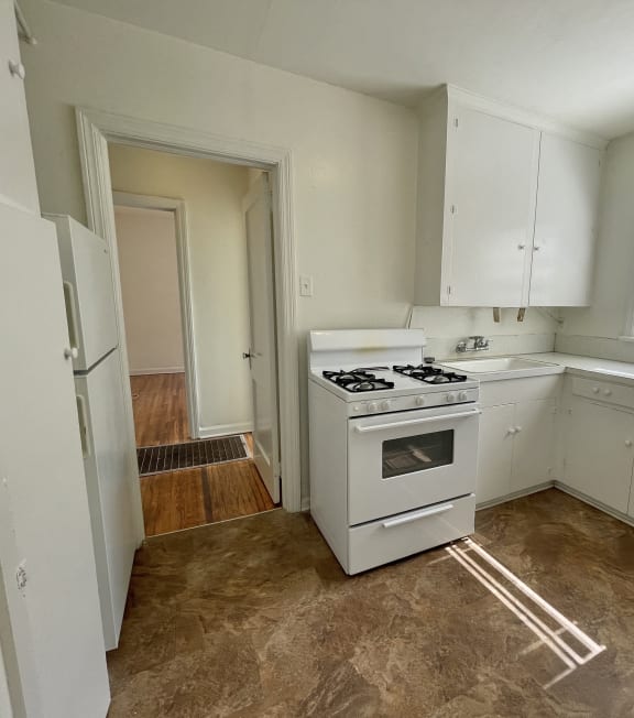 an empty kitchen with white cabinets and a stove and a window