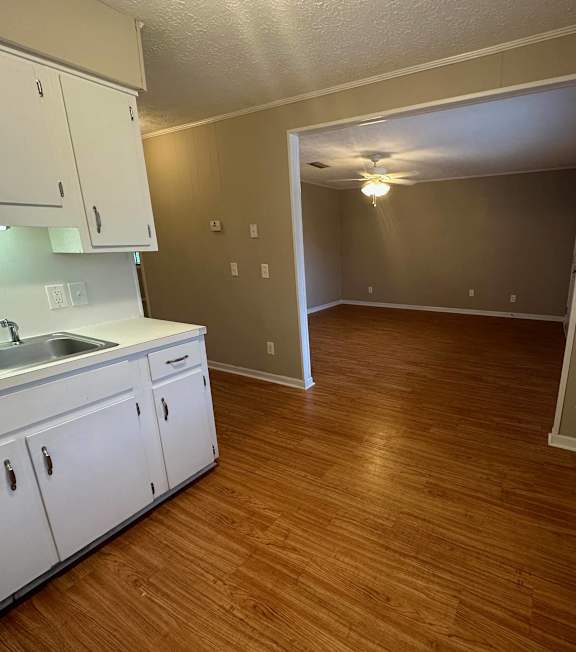 an empty kitchen and living room with wood flooring and white cabinets