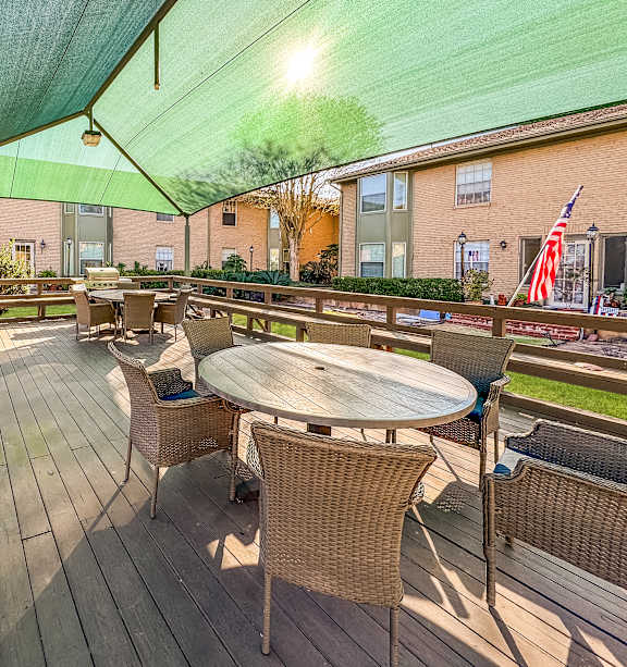 A wooden deck with a table and chairs under a green canopy.