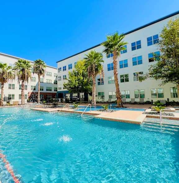 A large swimming pool in front of a white building with palm trees.